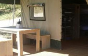 Vista interior y exterior de la tienda Safari en Agricamping Romita, Italia, con mesa y banco de madera.