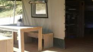 Vista interna ed esterna della tenda Safari all’Agricamping Romita in Italia, con tavolo e panche in legno.