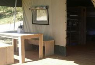 Vista interior y exterior de la tienda Safari en Agricamping Romita, Italia, con mesa y banco de madera.