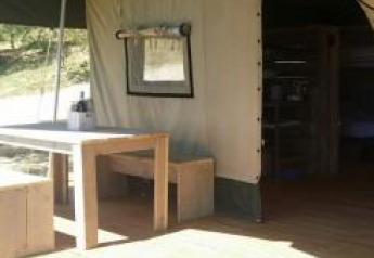 Binnen- en buitenaanzicht van de safaritent bij Agricamping Romita in Italië met houten tafel en bank.
