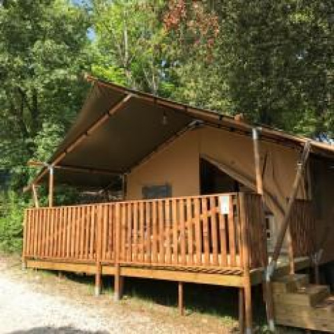 Tienda safari con instalaciones sanitarias y terraza de madera en Camping Mar y Sierra, rodeada de árboles.