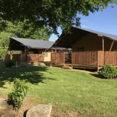 Tienda safari con instalaciones sanitarias en Camping de Kerleyou en Francia, rodeada de césped verde y árboles.