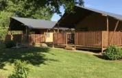 Tienda safari con instalaciones sanitarias en Camping de Kerleyou en Francia, rodeada de césped verde y árboles.