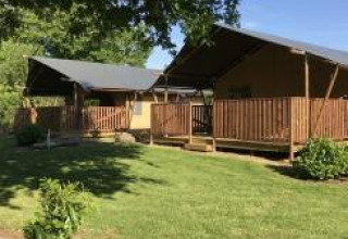 Tienda safari con instalaciones sanitarias en Camping de Kerleyou en Francia, rodeada de césped verde y árboles.