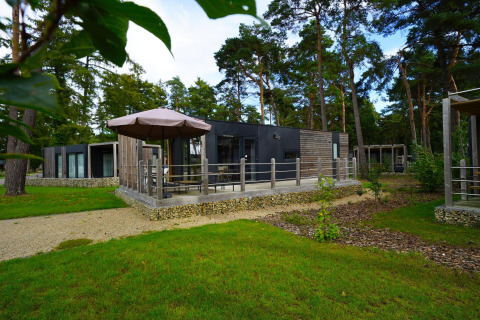 Cabaña moderna Heiberg en Hoge Kempen, Bélgica, con terraza, sombrilla y rodeada de bosque verde.