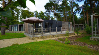 Chalet Heiberg moderne au Hoge Kempen, Belgique, avec terrasse et parasol, entouré de forêt verdoyante.