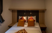 Sfeervolle slaapkamer met dubbel bed, kleurrijke kussens en leeslampjes in Heiberg cottage, Hoge Kempen.
