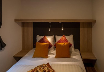 Sfeervolle slaapkamer met dubbel bed, kleurrijke kussens en leeslampjes in Heiberg cottage, Hoge Kempen.