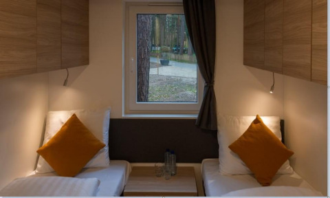 Binnenzicht in Heiberg cottage, Hoge Kempen, België, met twee bedden, kussens en zicht op het bos.