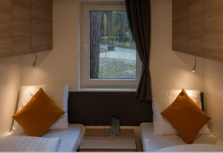 Vista interior de Heiberg cottage en Hoge Kempen, Bélgica, con dos camas, almohadas y ventana al bosque.