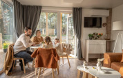 Gezin dineert samen in Heiberg cottage in Hoge Kempen, België, met uitzicht op het bosrijke landschap.