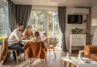 Gezin eet samen in het knusse Heiberg cottage in Hoge Kempen, België, met zicht op de natuur.