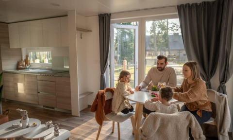 Una familia comparte una comida en la cabaña Heiberg en Hoge Kempen, Bélgica, ambiente acogedor.