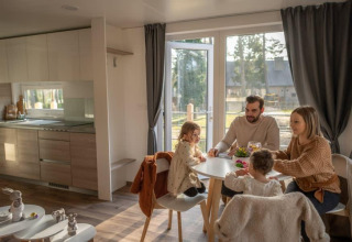 Una familia comparte una comida en la cabaña Heiberg en Hoge Kempen, Bélgica, ambiente acogedor.