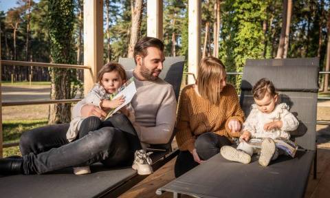 Una familia se relaja al aire libre en Heiberg cottage, Hoge Kempen, Bélgica, rodeada de bosque hermoso.