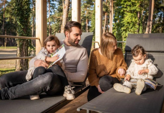 Familie entspannt auf der Terrasse des Heiberg Cottage in Hoge Kempen, Belgien, mit Wald im Hintergrund.