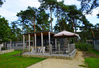 Vista exterior de la cabaña Heiberg con terraza y sombrilla rodeada de árboles en Hoge Kempen, Bélgica