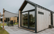 Tiny House XL moderno en Camping Si-Es-An, Países Bajos, con grandes ventanales y terraza exterior amueblada.