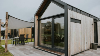 Modern Tiny House XL at Camping Si-Es-An in the Netherlands, featuring large windows and a patio area.