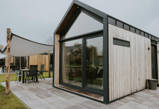 Moderne Tiny House XL bij Camping Si-Es-An in Nederland met grote ramen en een ingericht terras.