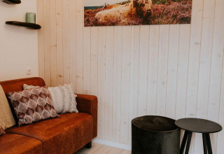 Gezellige woonkamer in Tiny house XL bij Camping Si-Es-An, Nederland, met een bruine zetel en koeienkunst.