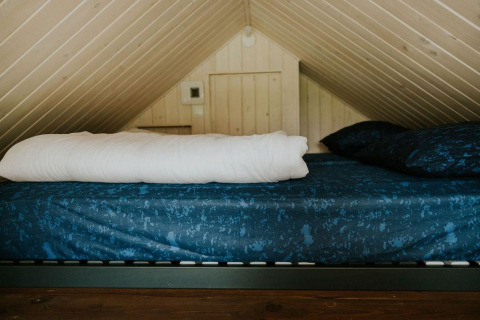 Cozy loft bed with blue bedding in Tiny House XL at Camping Si-Es-An, Netherlands, under sloped ceiling.