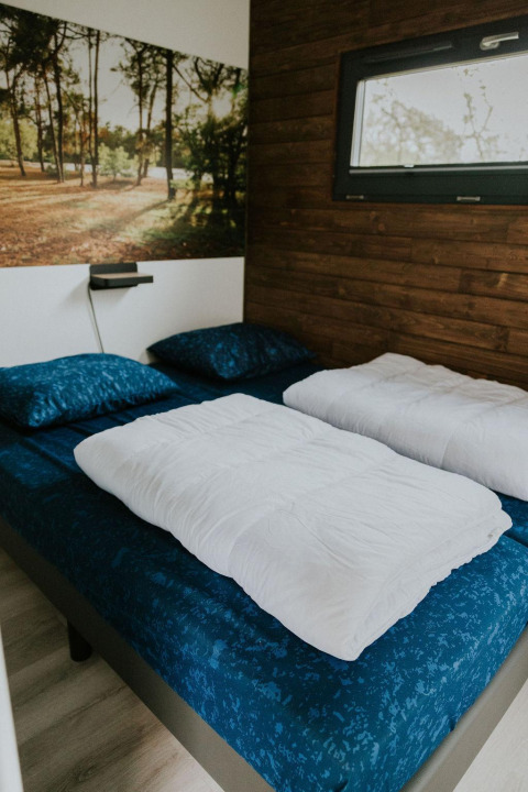 Camera da letto nel Tiny house XL al Camping Si-Es-An, Paesi Bassi, con parete in legno e murale naturale.