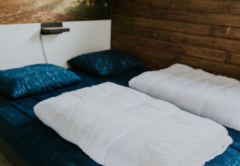 Camera da letto nel Tiny house XL al Camping Si-Es-An, Paesi Bassi, con parete in legno e murale naturale.