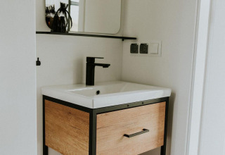 Moderne lavabo met houten kastje en zwarte kraan in Tiny house XL op Camping Si-Es-An, Nederland.