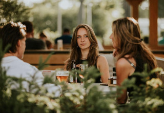 Drie mensen zitten buiten aan een tafel met drankjes bij Tiny house XL op Camping Si-Es-An, Nederland.