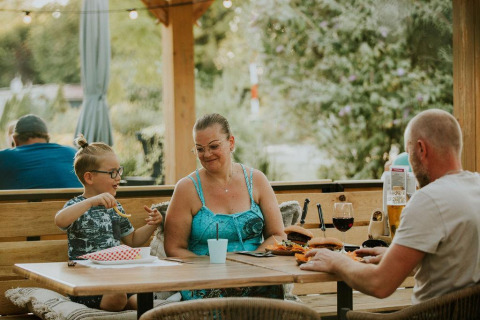 Famille prenant un repas en plein air au Tiny house XL au Camping Si-Es-An aux Pays-Bas, entourée de verdure.