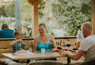 Famille prenant un repas en plein air au Tiny house XL au Camping Si-Es-An aux Pays-Bas, entourée de verdure.