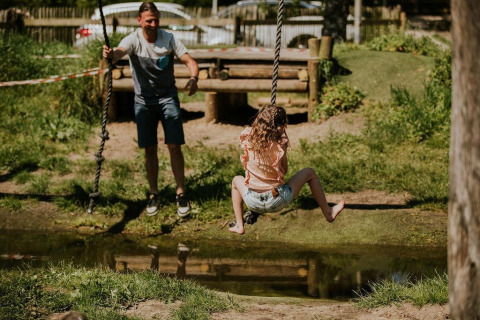Uomo spinge una ragazza su un’altalena di corda sopra uno stagno a Tiny house XL, Camping Si-Es-An, Paesi Bassi.