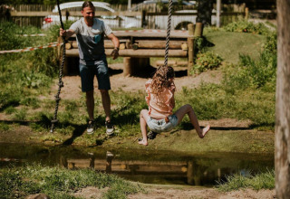 Mann schubst ein Mädchen auf einer Seilschaukel über einen Teich bei Tiny house XL, Camping Si-Es-An.