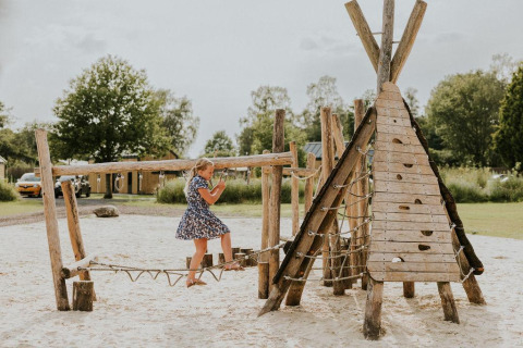 Niña juega en parque infantil de madera en Tiny house XL en Camping Si-Es-An, Países Bajos.