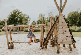 Meisje speelt op houten speeltuin bij Tiny house XL op Camping Si-Es-An in Nederland.