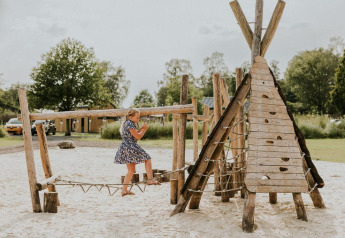Girl plays on a wooden playground at Tiny house XL, Camping Si-Es-An, Netherlands, on a sunny day.