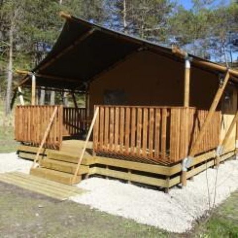 Tienda safari con terraza de madera en Camping Lou Passavous, Francia, rodeada de árboles y naturaleza.