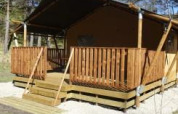 Tienda safari con terraza de madera en Camping Lou Passavous, Francia, rodeada de árboles y naturaleza.