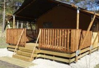 Tienda safari con terraza de madera en Camping Lou Passavous, Francia, rodeada de árboles y naturaleza.