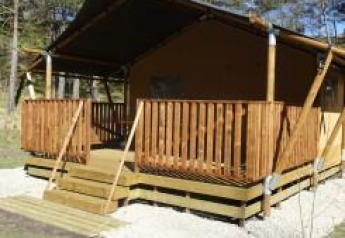 Tienda safari con terraza de madera en Camping Lou Passavous, Francia, rodeada de árboles y naturaleza.