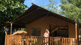 Tenda safari con servizi igienici al Camping Saint Amand in Francia, persona in piedi sulla veranda al sole.