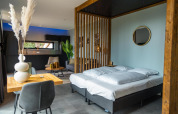 Modern ingerichte lodgekamer in Modus Wellness, Hoge Kempen, België, met bed, keuken en stijlvolle meubels.