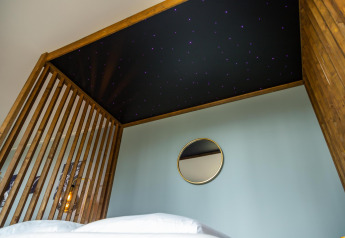 Slaapkamer met sterrenhemelplafond, houten structuur en wandspiegel in Modus Wellness Lodge, Hoge Kempen, België.