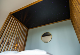 Dormitorio con techo de cielo estrellado, estructura de madera y espejo en la pared en Modus Wellness Lodge, Hoge Kempen, Bélgica.