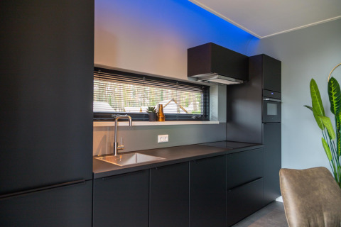 Cocina moderna negra con fregadero, horno y ventana en la cabaña Modus Wellness en Hoge Kempen, Bélgica.