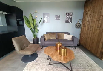 Moderne woonkamer in Modus Wellness Lodge, Hoge Kempen, België, met grijze zetel en houten tafel.