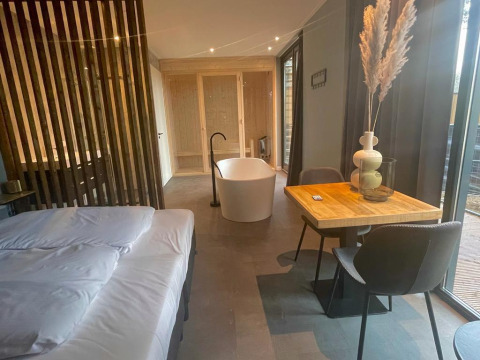 Moderna cabaña en Modus Wellness, Hoge Kempen, Bélgica, con cama, bañera independiente y mesa comedor.