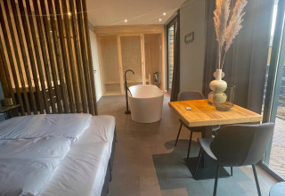 Lodge moderno a Modus Wellness, Hoge Kempen, Belgio con letto, vasca indipendente e tavolo da pranzo.