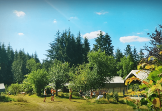 Familier hygger sig udendørs på Camping Domaine La Chabanne, omgivet af træer i Auvergne-Rhône-Alpes.